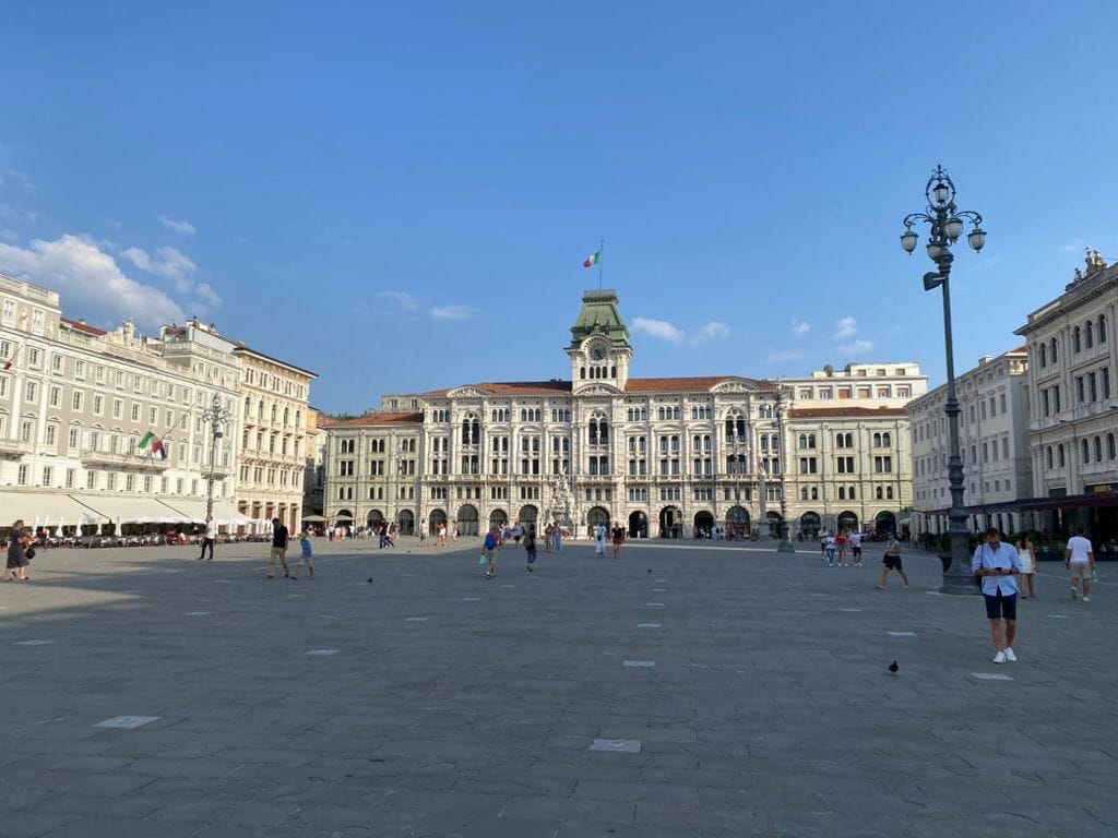 Großer Platz in Triest mit Palästen und einem Gebäude mit Uhrturm unter blauem Himmel