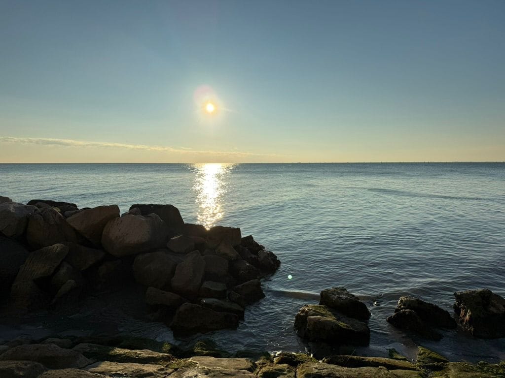 Felsen am Meer, die tief stehende Sonne spiegelt sich im Wasser